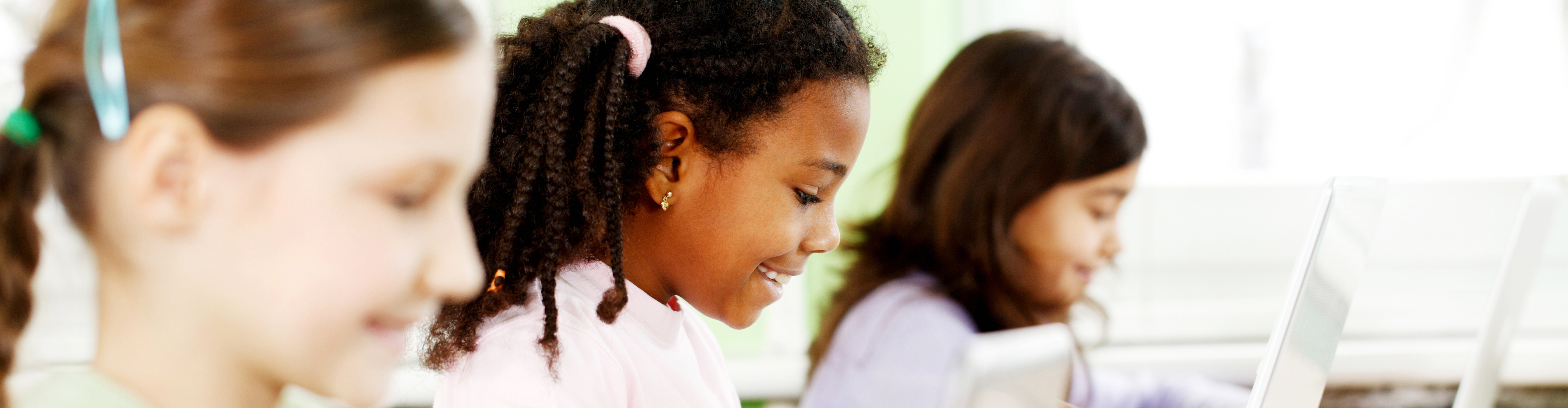 Three smiling girls using laptops in the classroom.